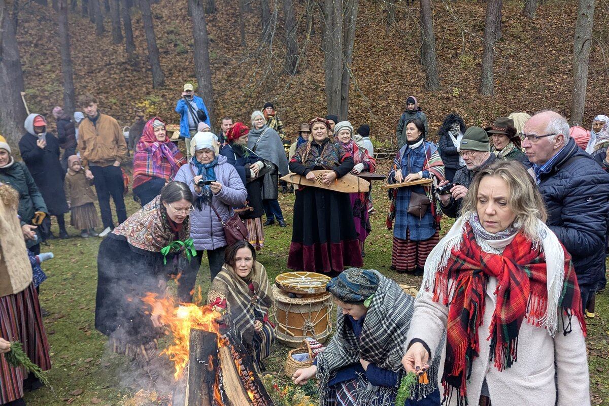 Besökare i folkdräkt runt en Mārtiņdiena-brasa på Lettlands etnografiska friluftsmuseum, Riga.