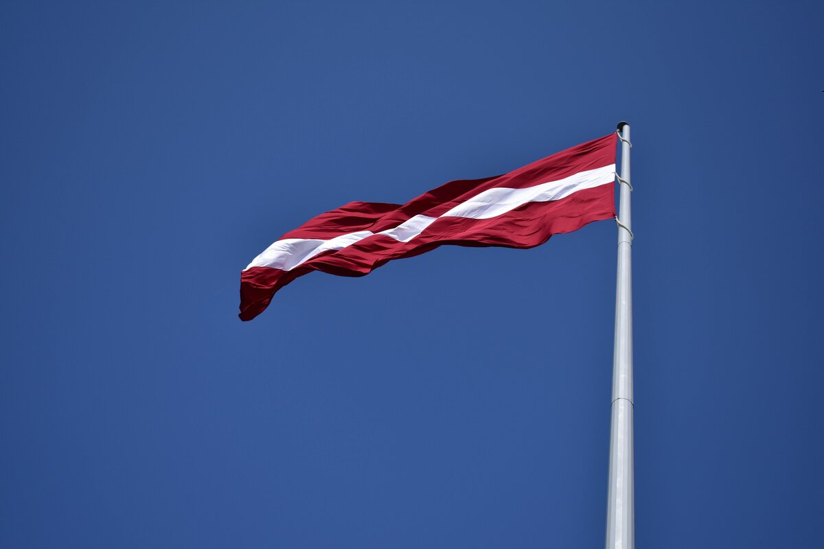 Lettlands flagga, karminröd med ett vitt band, vajande mot en blå himmel.