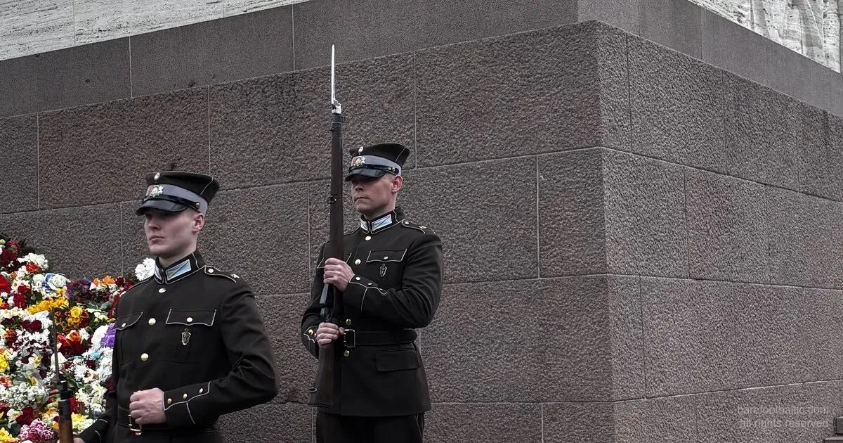 Lettiska arméns hedersvakt vid Frihetsmonumentet med en vägg av blommor lagd mot basen, Riga, på dagen för återställd självständighet
