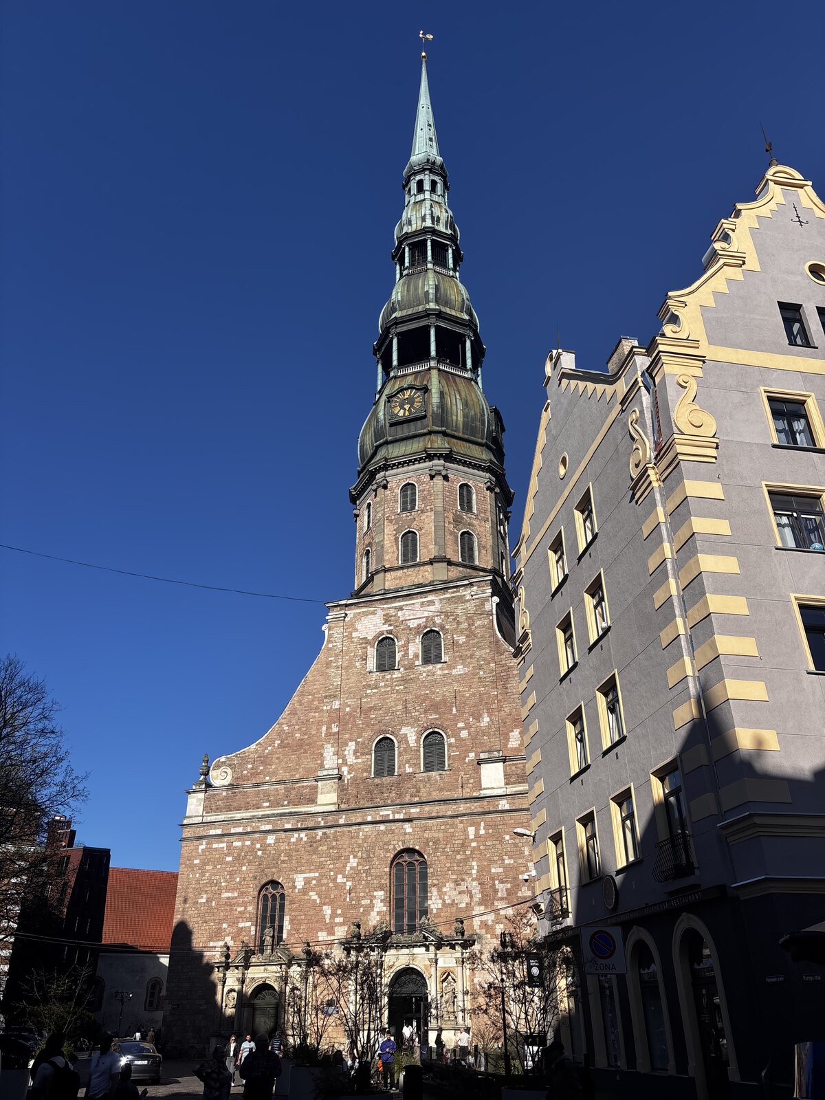 Sankt Peterskyrkan (Sv. Pētera baznīca) med sin höga gröna spira mot en blå himmel i Gamla stan i Riga, Lettland.