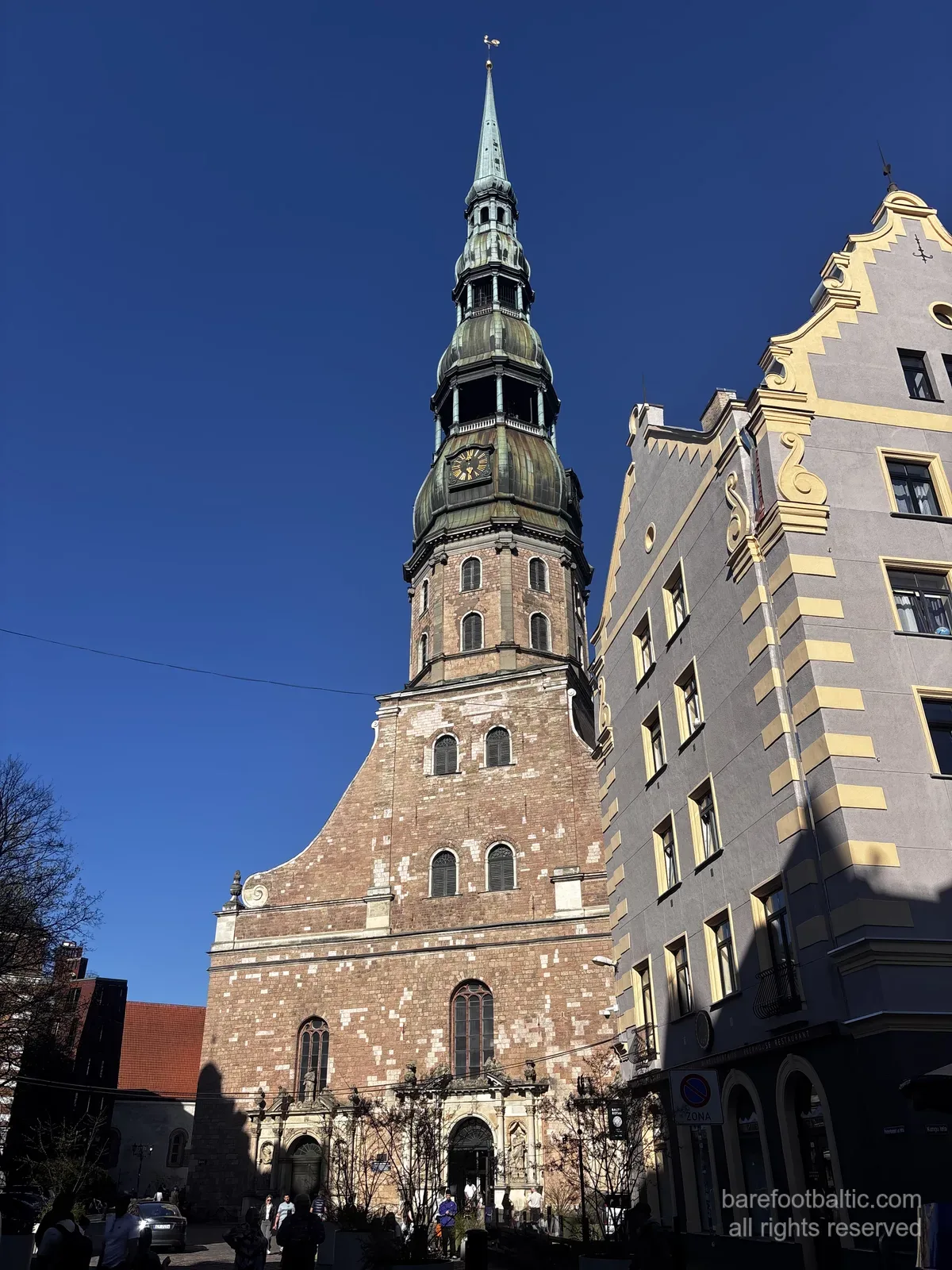 Sankt Peterskyrkan (Sv. Pētera baznīca) med sin höga gröna spira mot en blå himmel i Gamla stan i Riga, Lettland.