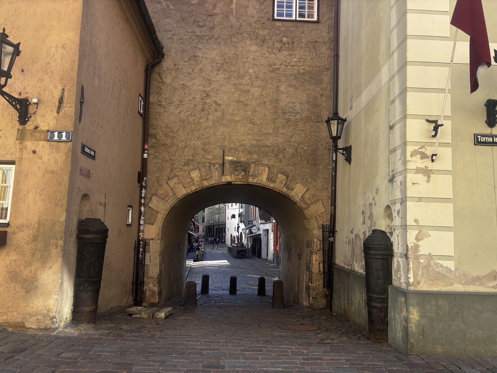 Svenska porten (Zviedru vārti) på Torņa iela i Rigas Gamla stan, Lettland, en stenvalvgång mellan två gula byggnader.