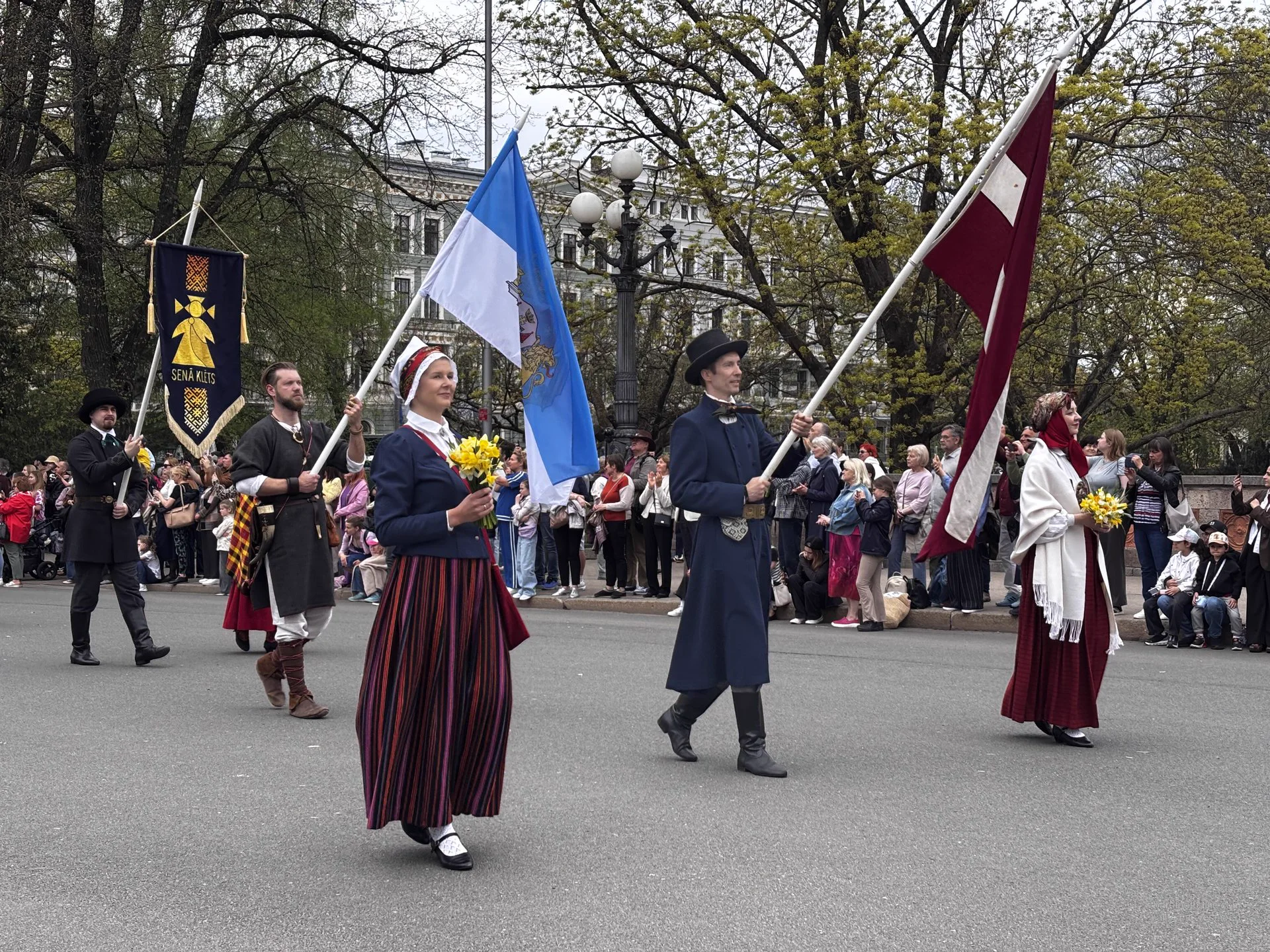 People in Latvian folk dress carrying flags during Independence Day celebrations in Riga