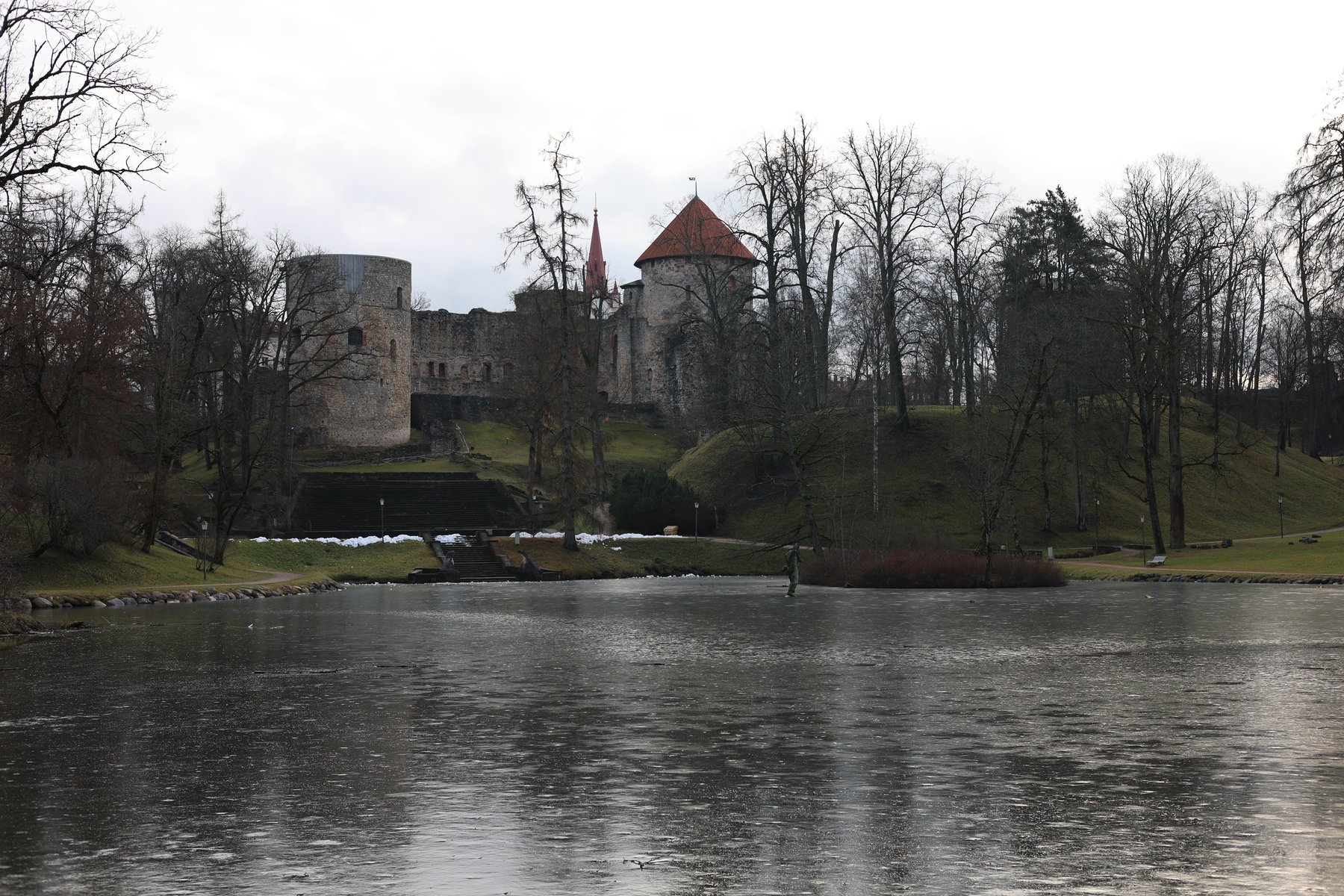 Cēsis slott speglat i en vinterkall damm med kala träd
