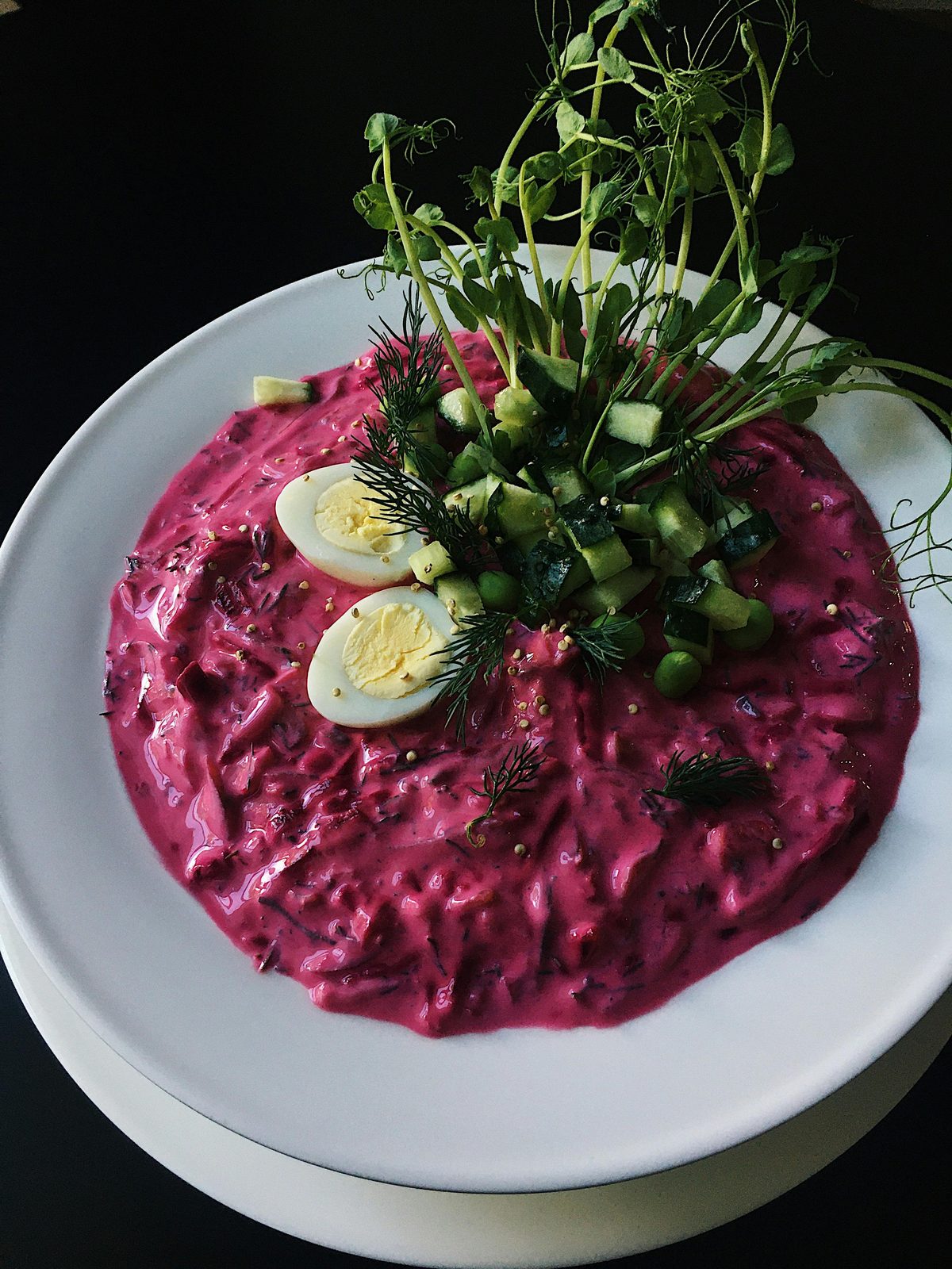 En skål knallrosa aukstā zupa, den lettiska kalla kefir-och-rödbetssommarsoppan, garnerad med hårdkokt ägg, gurka och dill