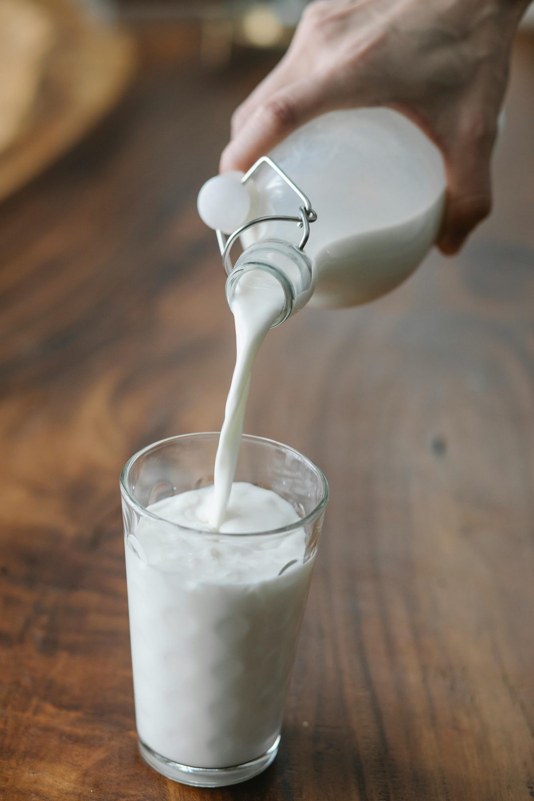 Lettisk kefir hälls från en flaska i ett glas på ett träbord