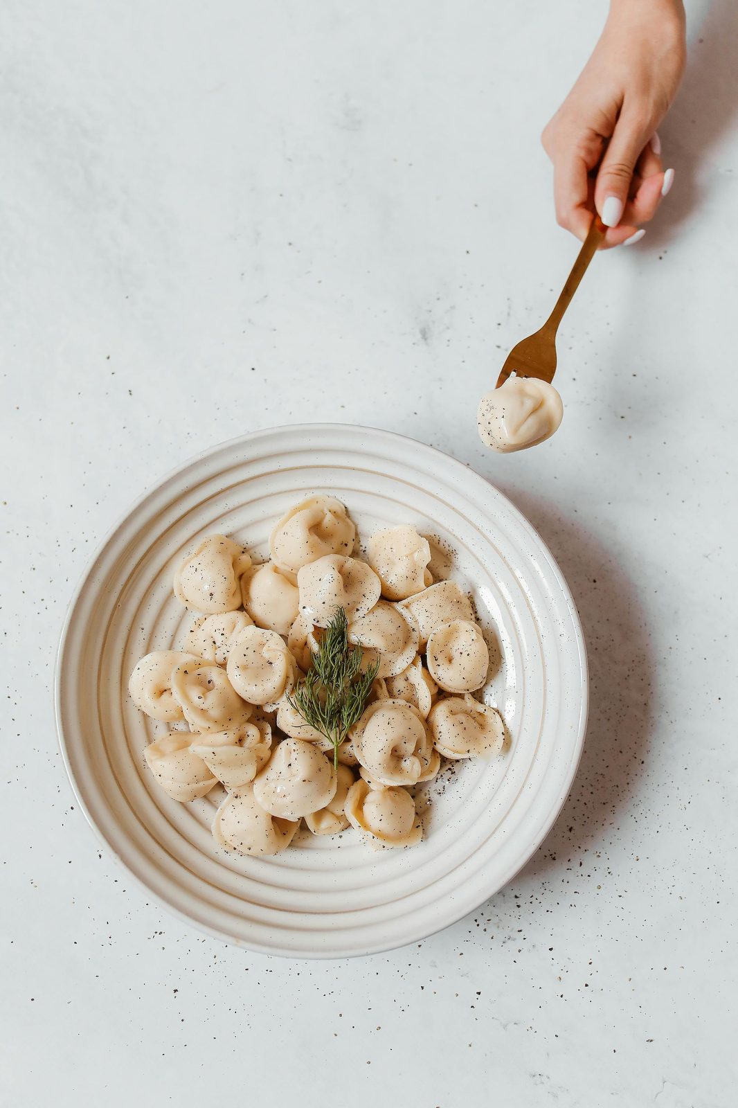 Pelmeņi dumplings på en vit tallrik med en dillkvist, en hand lyfter en med en gaffel