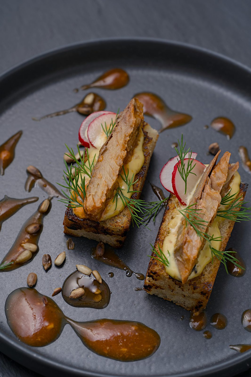 Förrätt med rökt fisk på rostat rågbröd med grädde, dill och rädisa, serverad på en svart tallrik