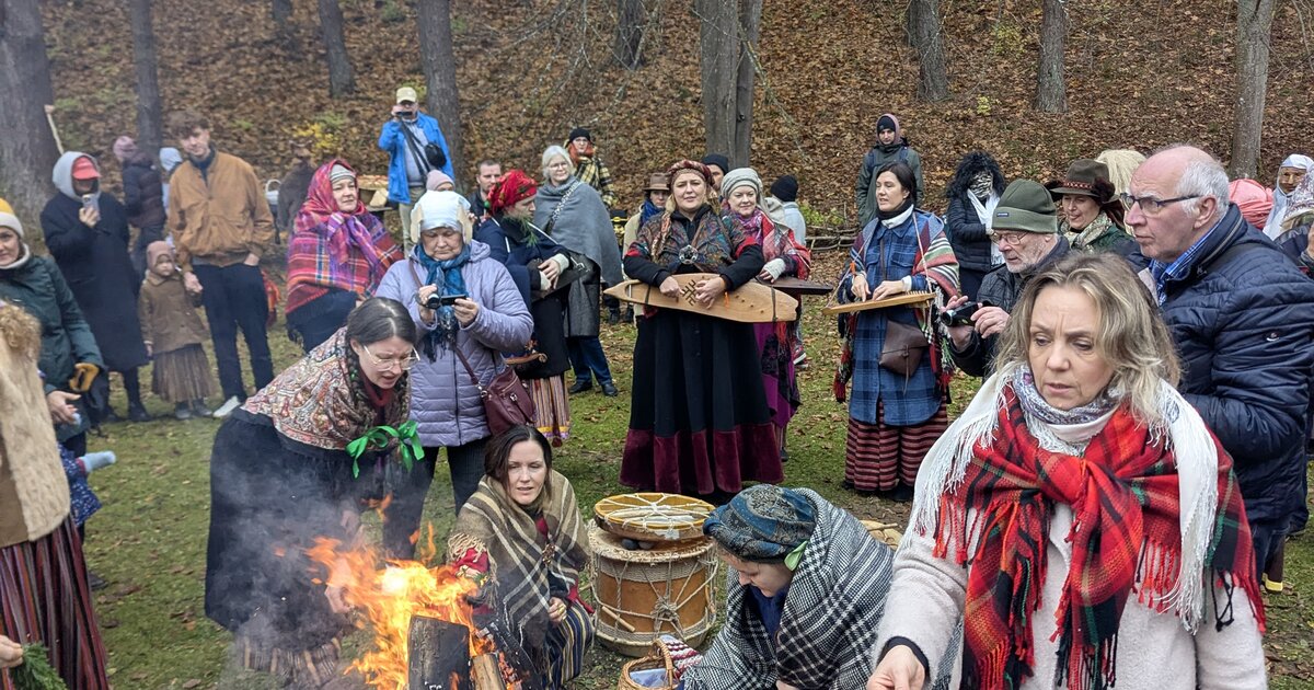 Besökare i folkdräkt runt en Mārtiņdiena-brasa vid Lettlands etnografiska friluftsmuseum, Riga.