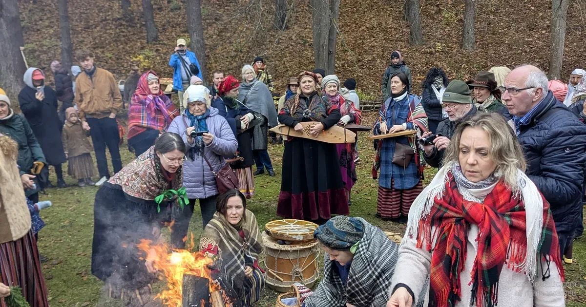 Besökare i folkdräkt runt en Mārtiņdiena-brasa vid Lettlands etnografiska friluftsmuseum, Riga.