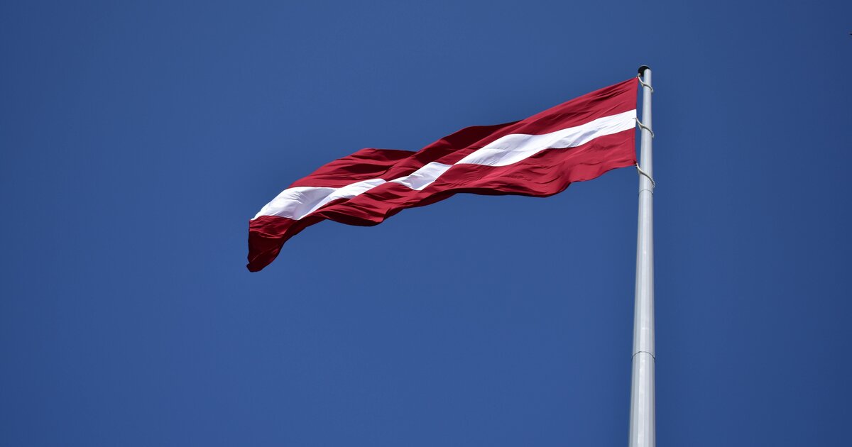 Den lettiska flaggan, karmosinröd med ett vitt band, som vajar mot en blå himmel.